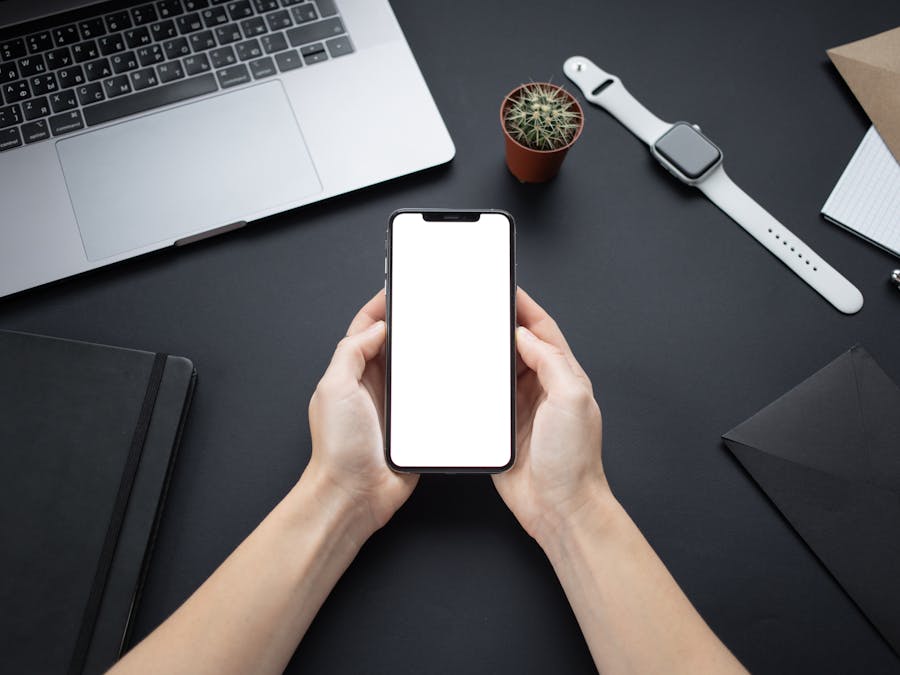 Hands holding a smartphone with blank screen on a minimalist office desk setup.