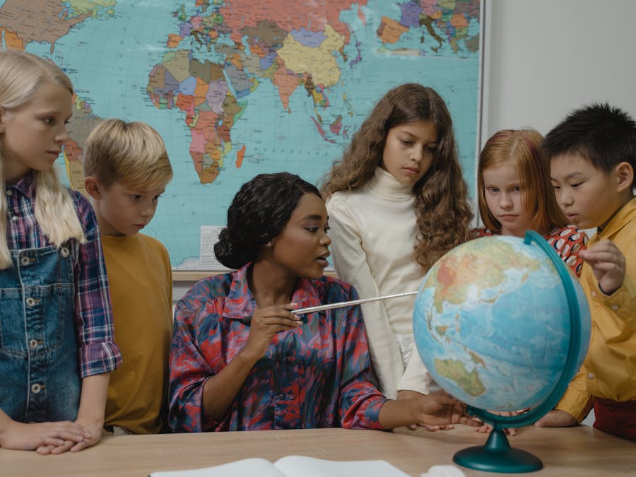 Diverse elementary students learning geography with a teacher and globe in the classroom.