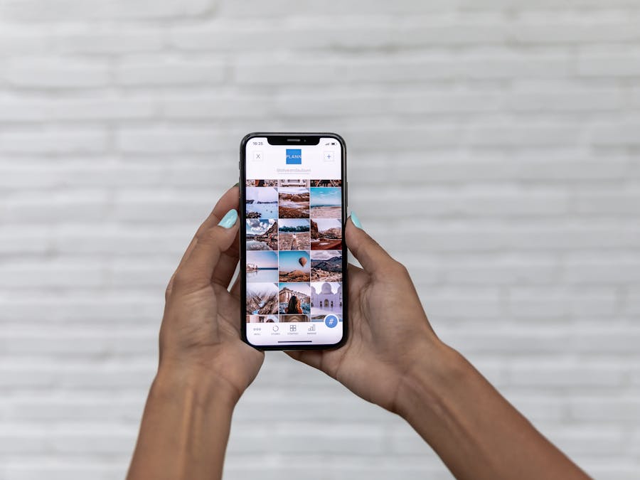 Close-up of woman holding a smartphone displaying a social media app against a brick wall.