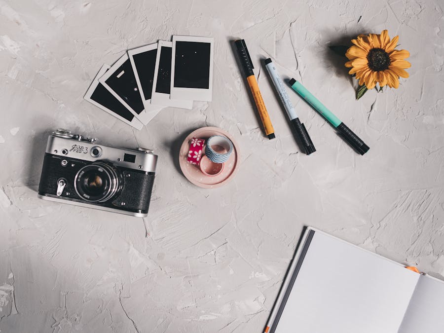 Flat lay of a creative workspace featuring a vintage camera, notebooks, and colorful pens.