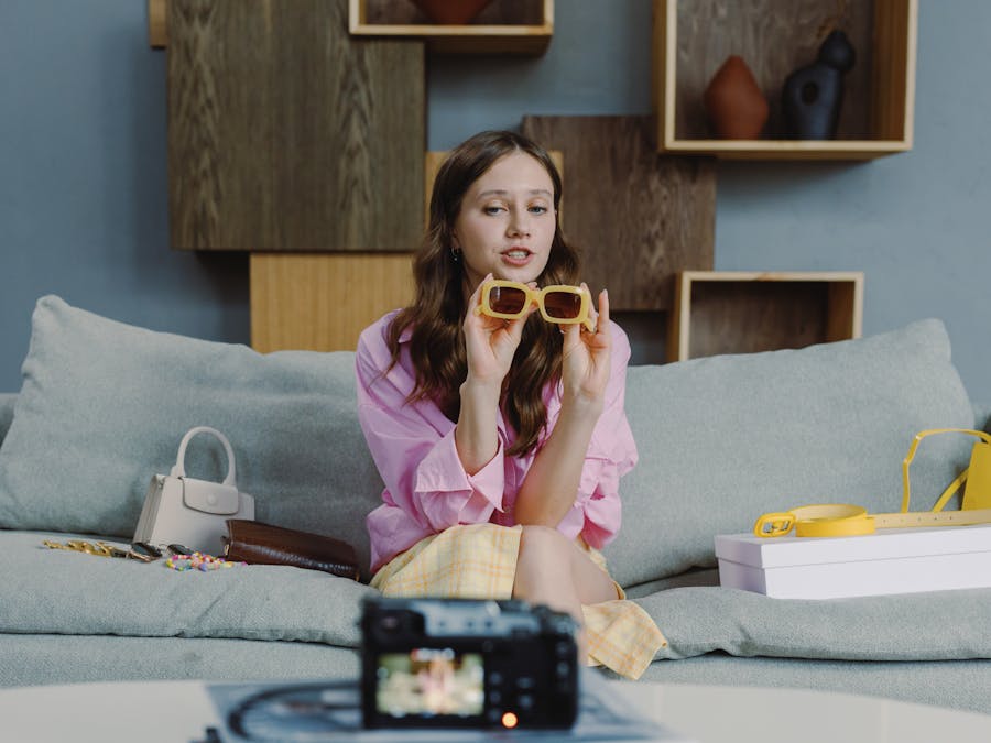 Young woman showcasing trendy sunglasses on a video blog at home.