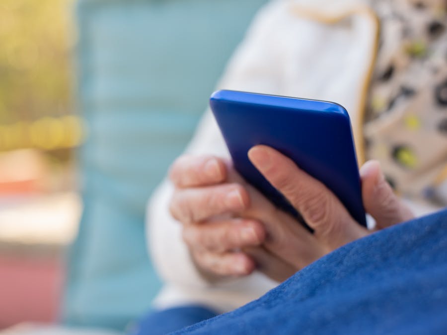 Senior adult using a smartphone outdoors on a sunny day. Focus on hands and device.