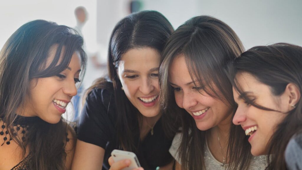 Four women smiling and looking at a smartphone together, creating a warm and joyful atmosphere.