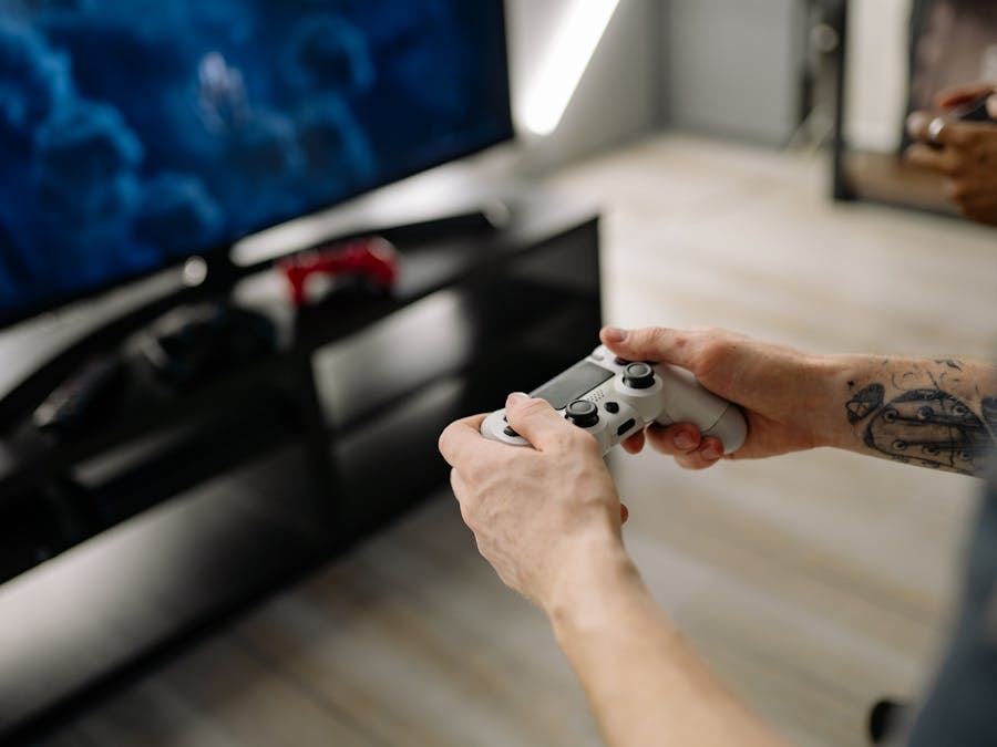 Person playing video games using a game controller indoors on a modern TV setup.
