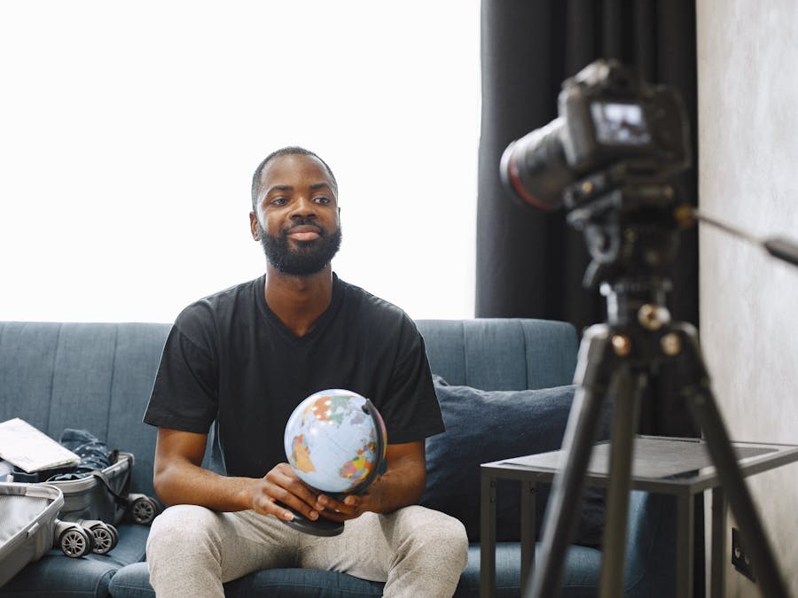 A man holding a globe sits in front of a camera, creating video content from his home studio.