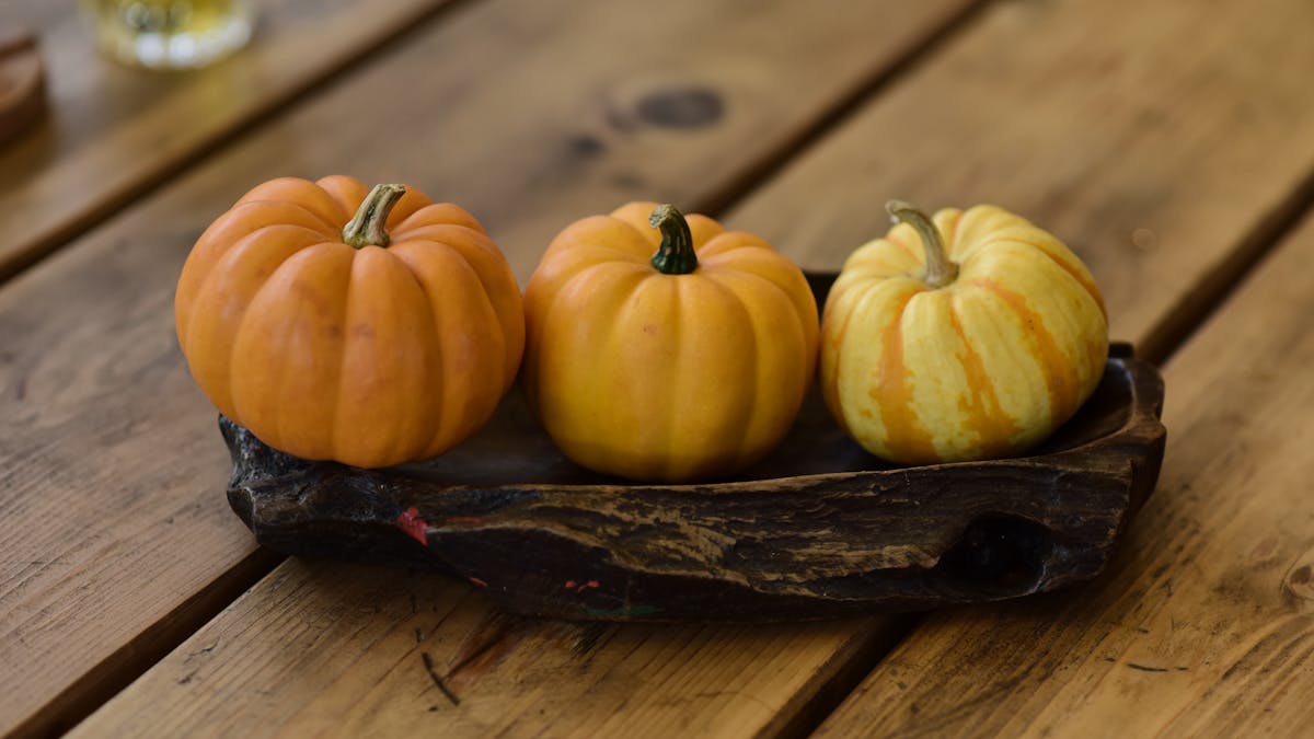 Three mini pumpkins on a wooden tray create a cozy autumn scene.
