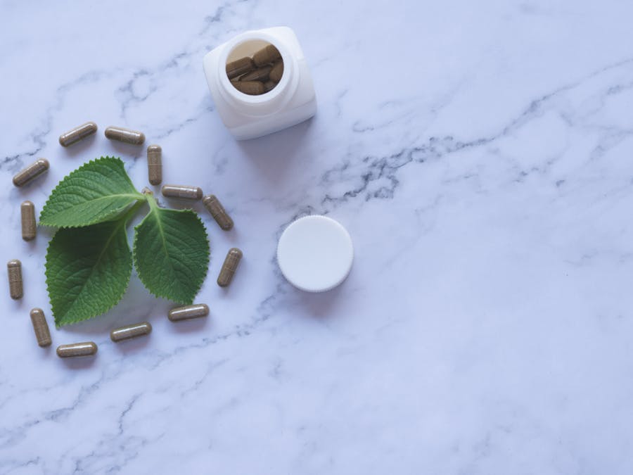 Flat lay of herbal capsules, leaves, and bottle on marble surface, symbolizing natural wellness.