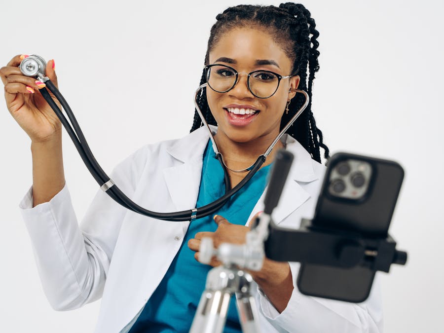 Young female doctor smiling while recording with smartphone and stethoscope.