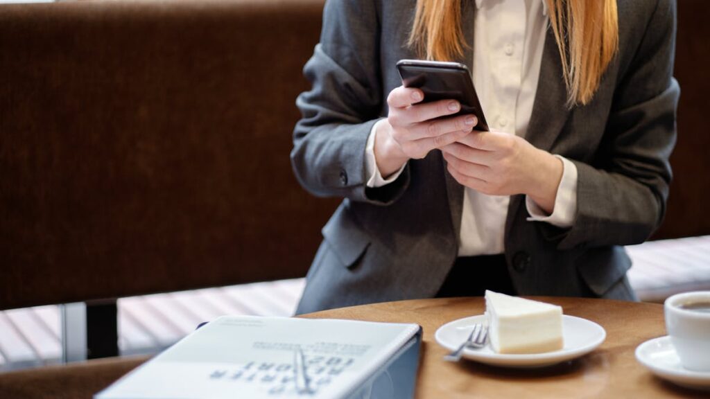 Businesswoman using smartphone in a café, with slice of cake and coffee.