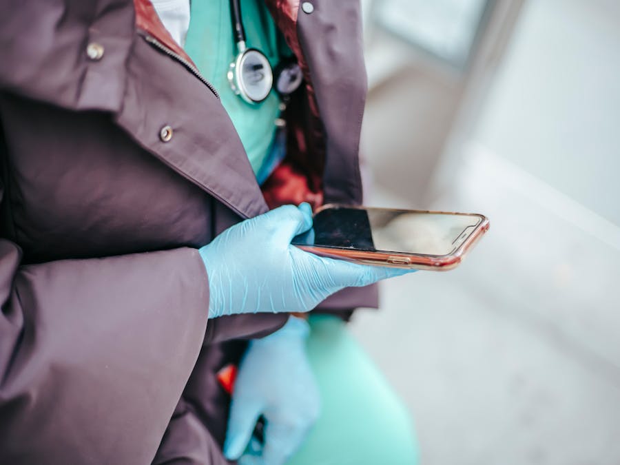 From above of crop unrecognizable female physician in outerwear touching black screen on mobile phone in daylight