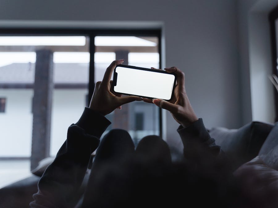 Person holding a smartphone while relaxing on the couch at home, blank screen.