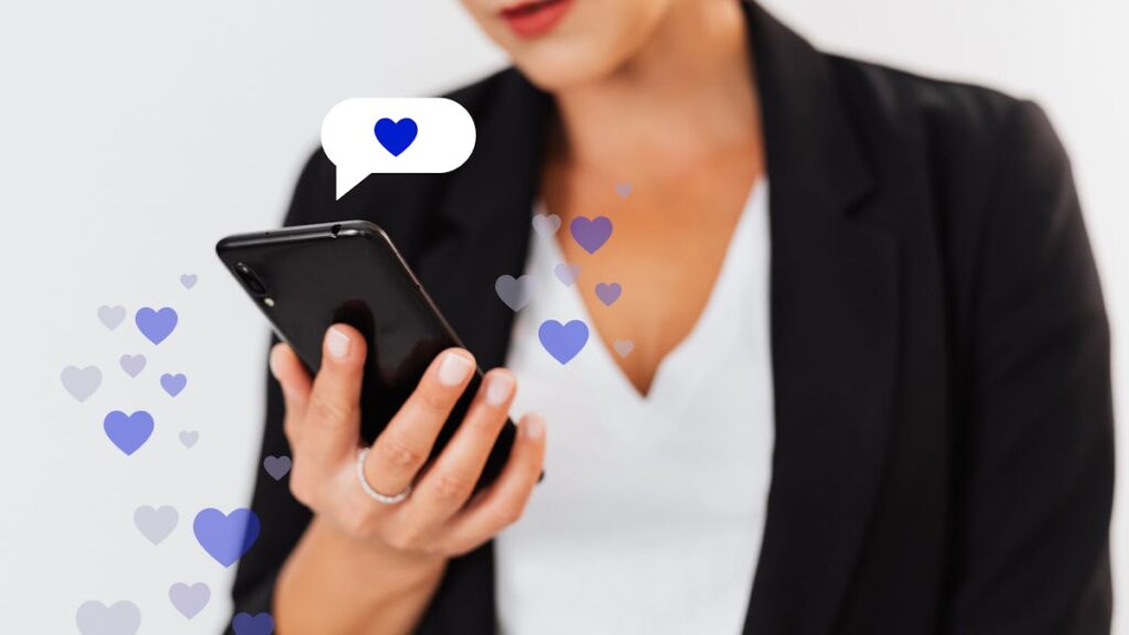 Close-up of a woman holding a smartphone with floating heart icons, illustrating digital engagement.