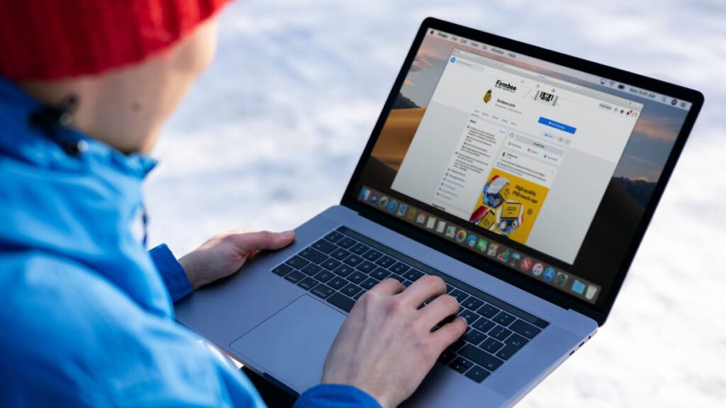 Close-up of individual using laptop outdoors in snow, browsing social media.