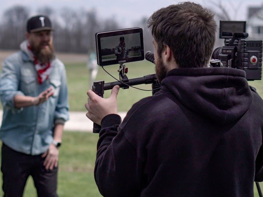 A cameraman films a music video scene outdoors in a field, with professional equipment.