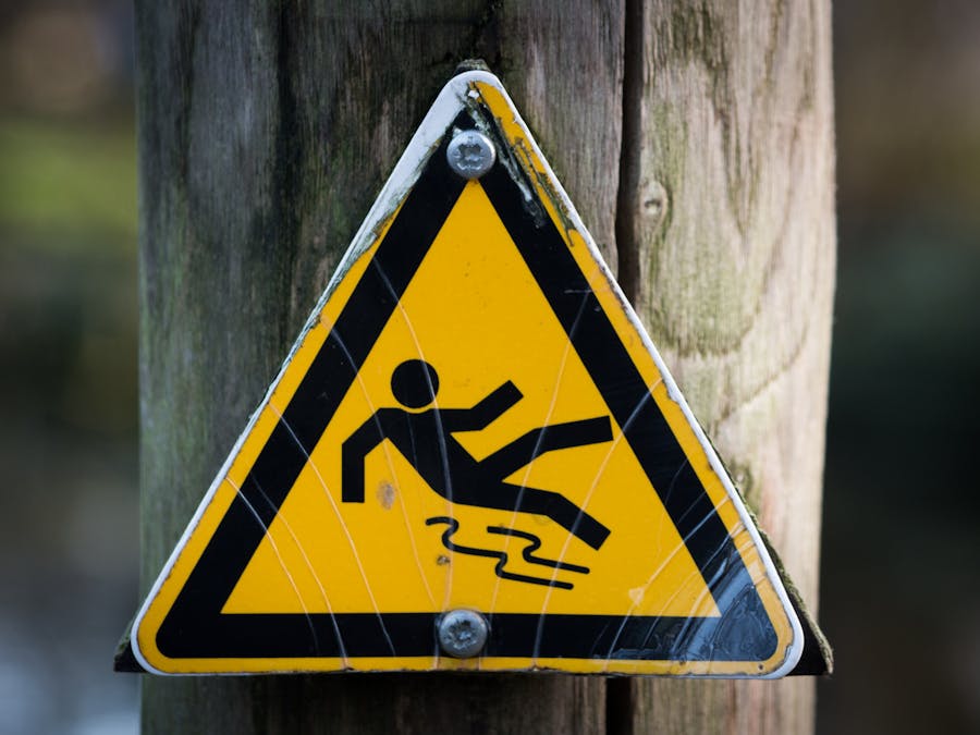 Close-up of a triangular warning sign indicating a slippery surface, fixed to a wooden post.