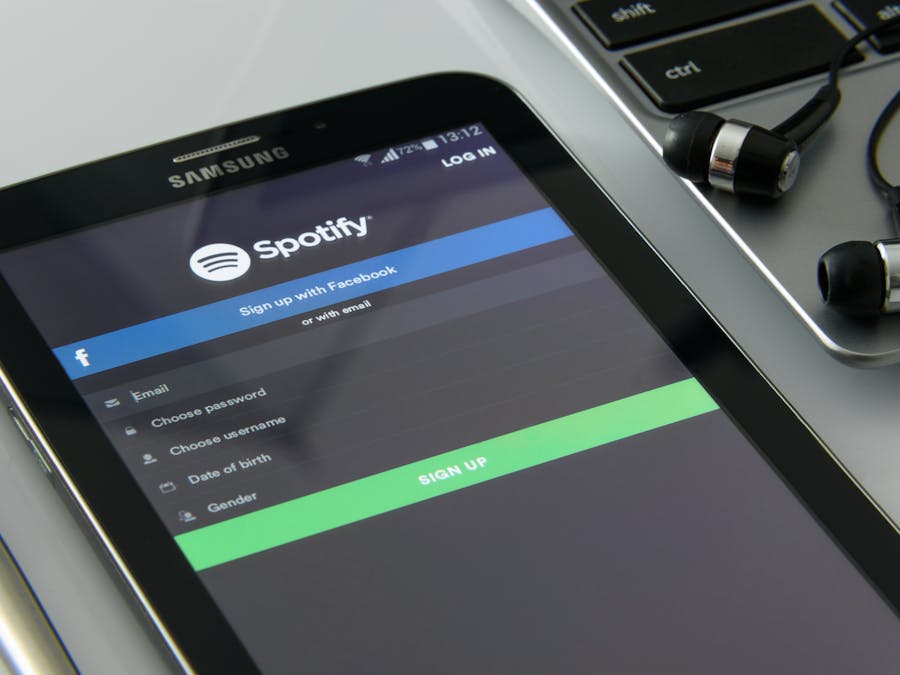 Smartphone showcasing Spotify login screen beside laptop and earphones on desk.