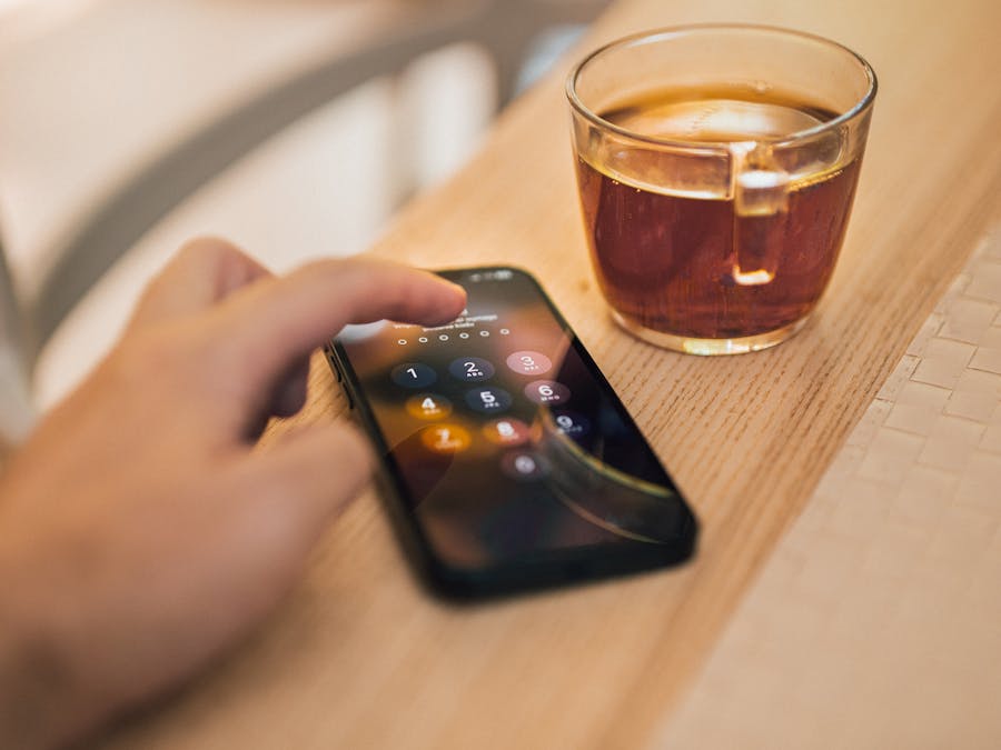 Close-up of hand unlocking a smartphone next to a cup of tea on a wooden table, emphasizing technology and security.