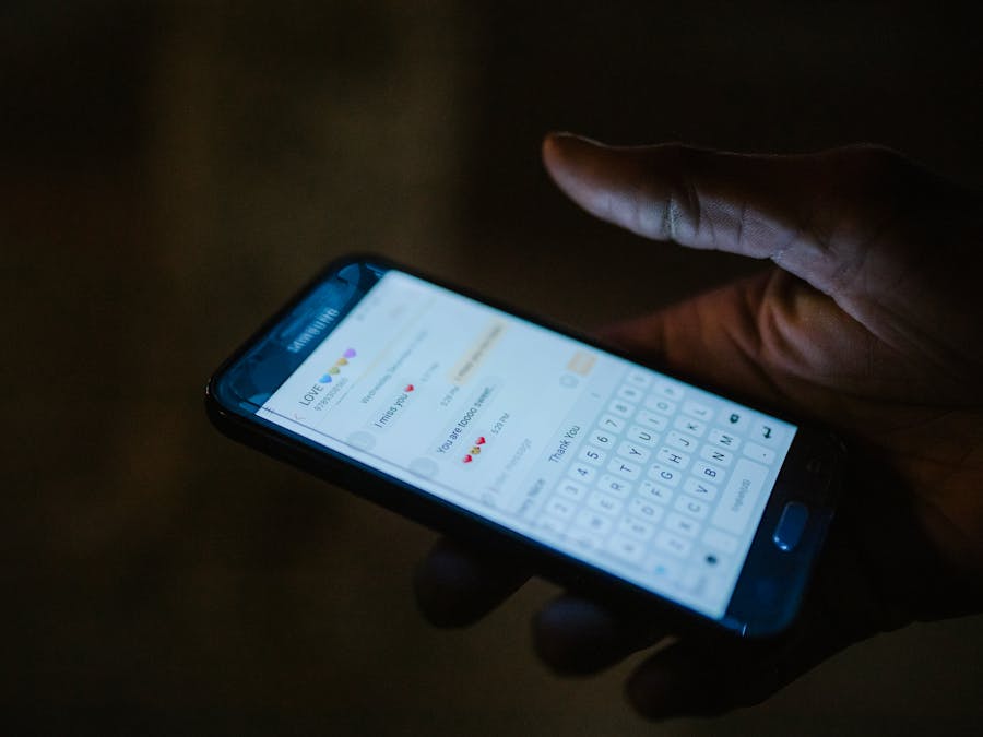Close-up of a hand holding a smartphone with a messaging app open, illuminated by screen light.