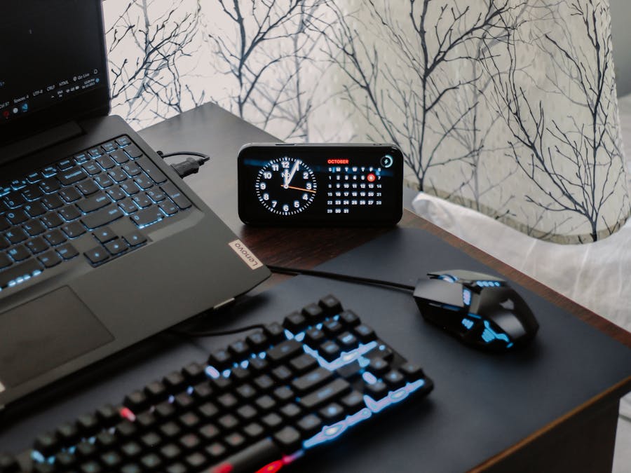 A modern workspace featuring a laptop, digital clock, gaming mouse, and keyboard, ideal for work and tech enthusiasts.