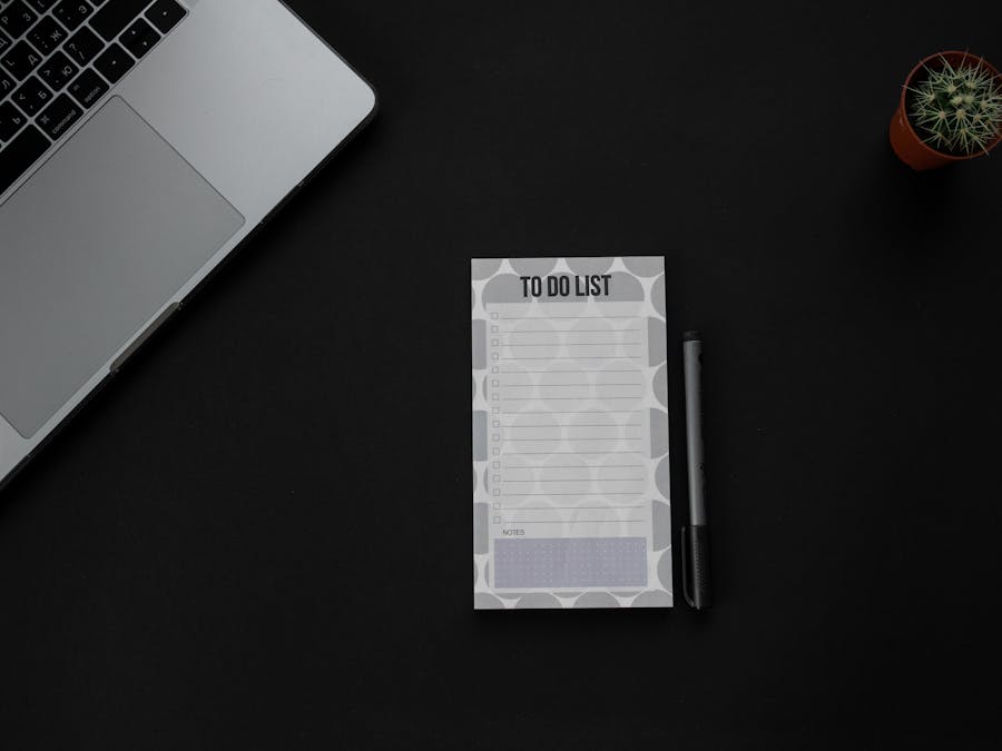 A minimalistic desk setup featuring a laptop, to-do list, and pen on a dark background. Ideal for productivity themes.