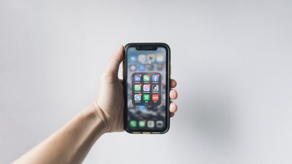 Hand holding smartphone displaying social media apps on home screen.