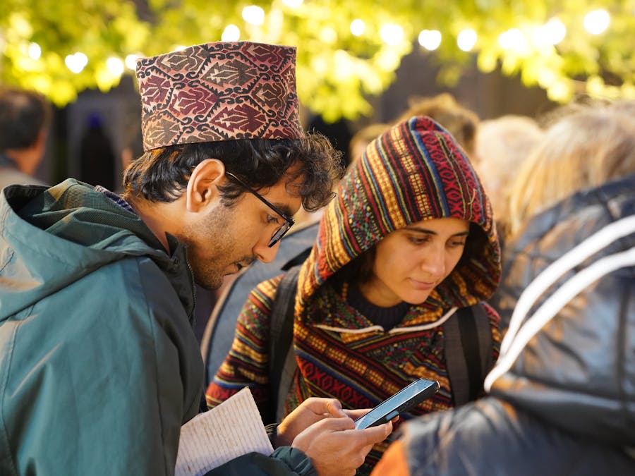 Two adults engaged with a smartphone at an outdoor social event under string lights.