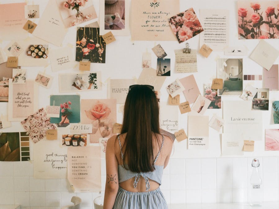 A woman with tattoos looks at a creative mood board filled with floral photos and quotes.