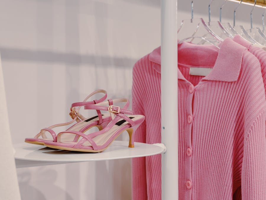 Elegant pink sandals and a knit sweater displayed on a shelf in a fashion boutique.