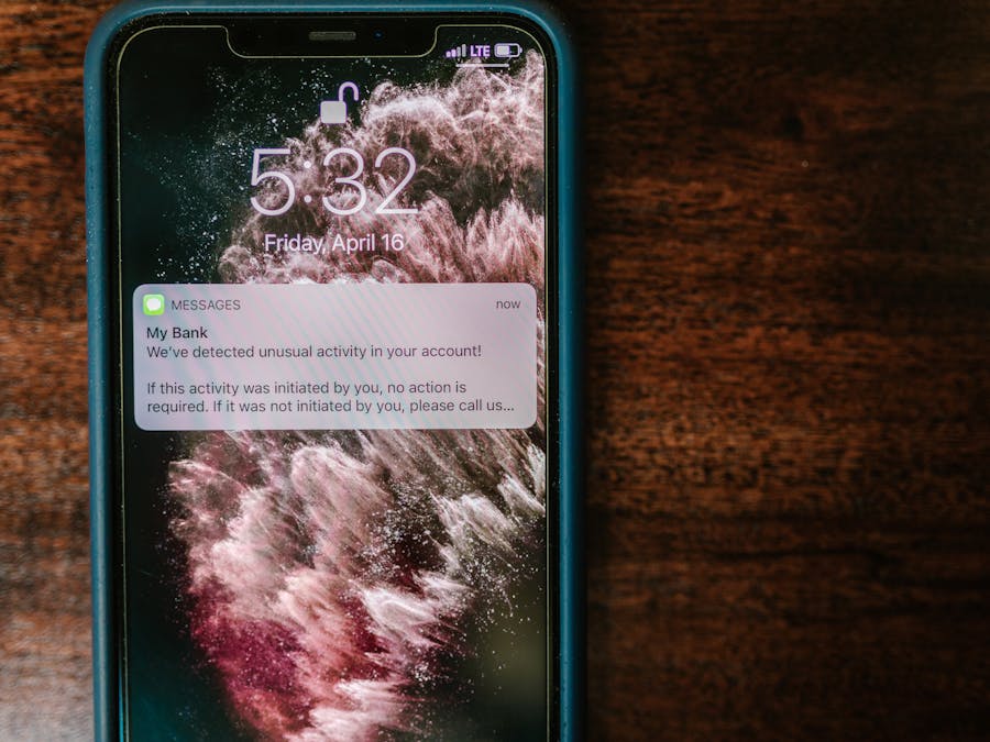 Close-up of a smartphone displaying a bank alert notification on a wooden table.