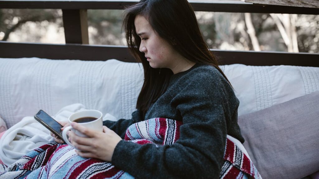 A woman enjoys a quiet moment with coffee and a phone on a cozy outdoor couch.