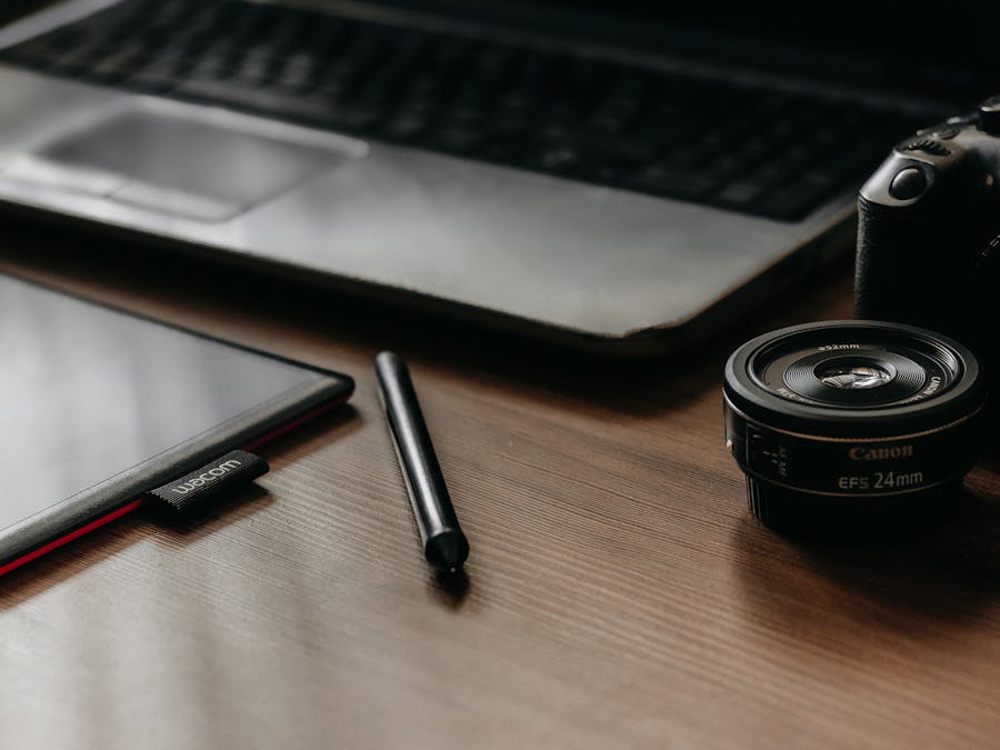 A workspace featuring a laptop, tablet, camera, and lens, ideal for creative work and photography.