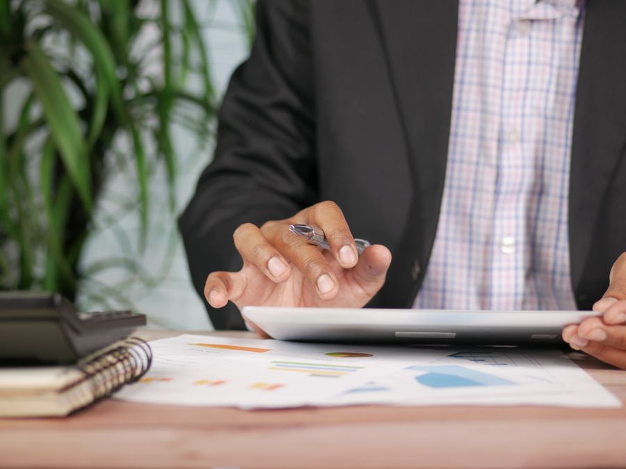Business professional in suit using tablet with pen on desk with documents and calculator.