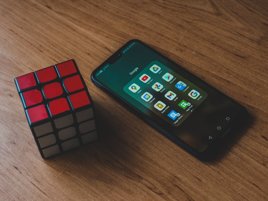 Close-up of smartphone with apps and a Rubik's Cube on a wooden table. Ideal for tech and leisure topics.