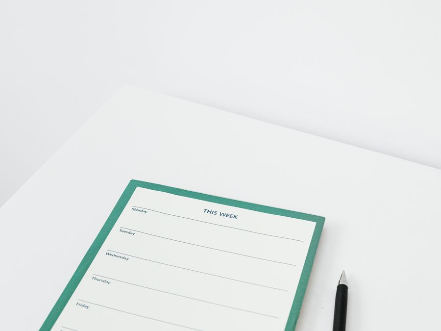 A clean and minimalist weekly planner with a pen on a white desk, perfect for organizing your schedule efficiently.