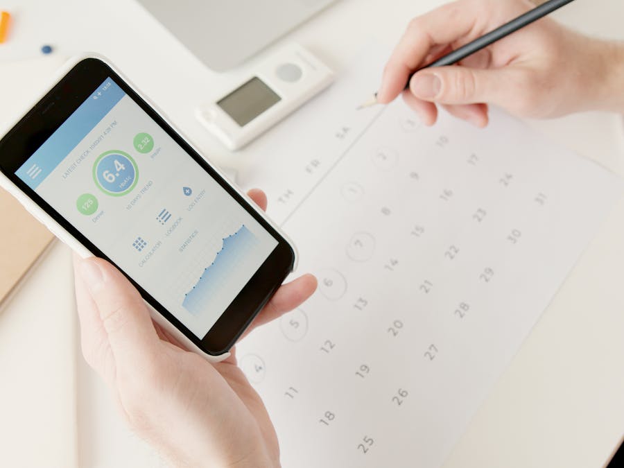 Close-up of hands using a smartphone to track health stats while planning on a calendar.