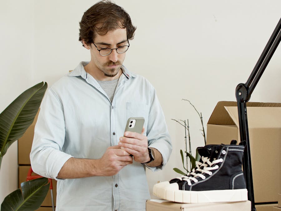 Man uses phone to photograph sneakers in an indoor business setup with boxes.