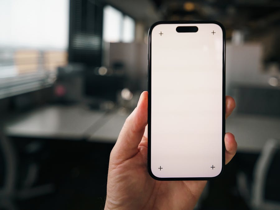 Hand holding a blank smartphone screen mockup in a modern office environment, perfect for apps showcasing.