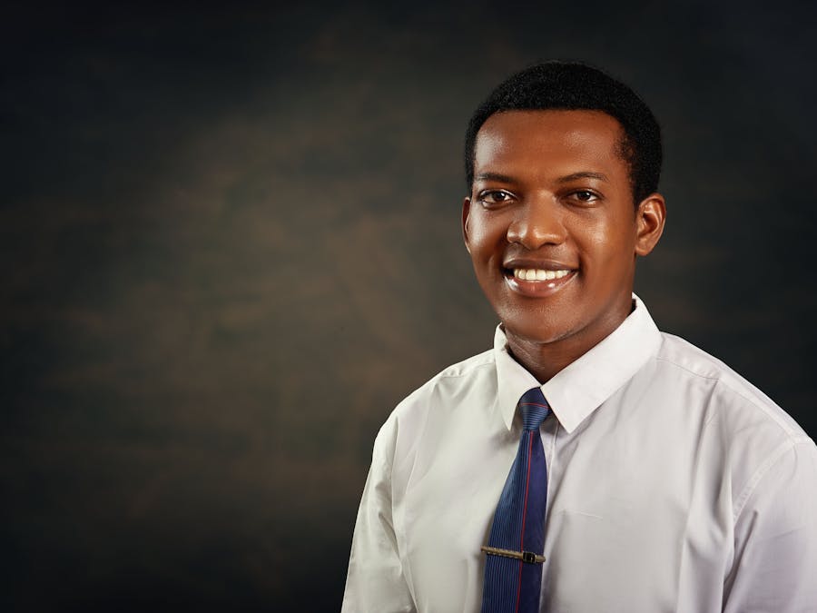 Smiling young adult man in formal attire against dark background, ideal for business or profile use.