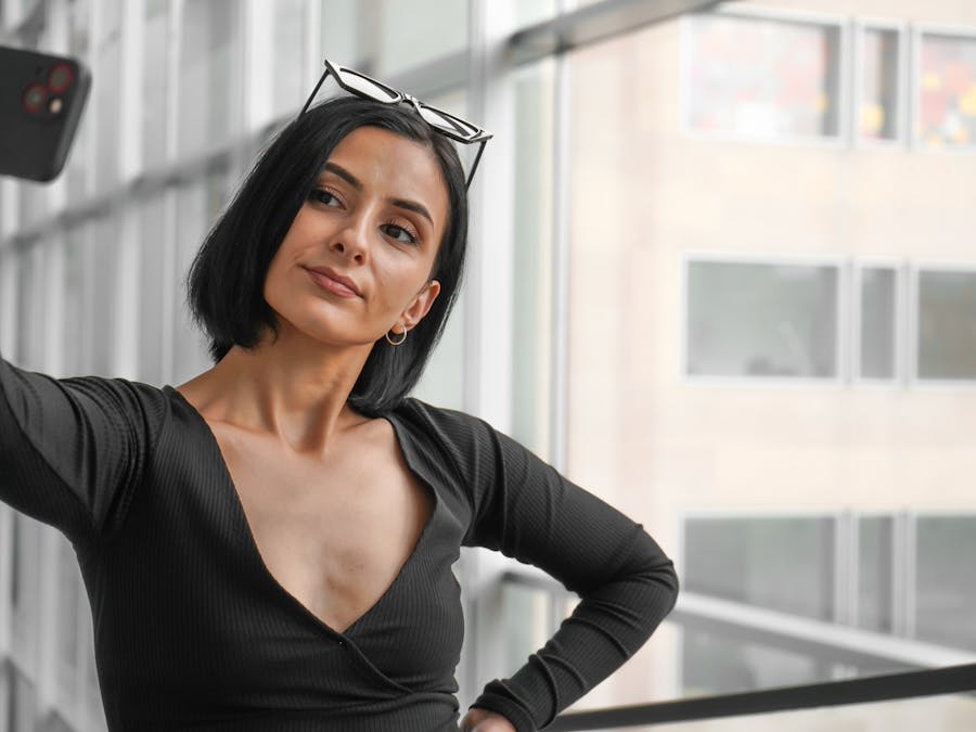 Confident woman in black outfit taking a selfie indoors with smartphone.