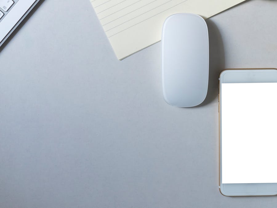 Contemporary workspace flat lay featuring a smartphone, wireless mouse, keyboard, and paper on a minimalist desk.