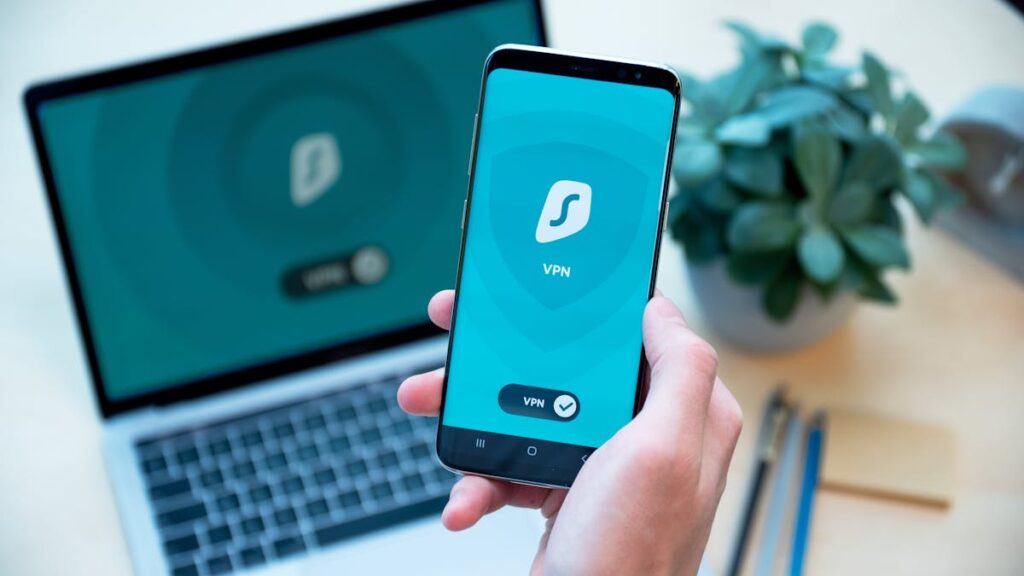 Close-up of a hand holding a smartphone with VPN app, laptop in the background, showcasing digital security.