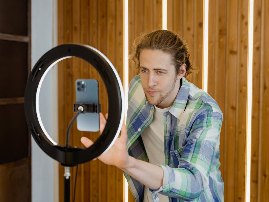 A young man sets up a smartphone and ring light for social media video recording, focusing on optimal lighting.