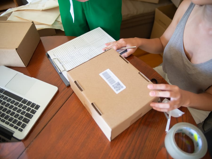 Two people packing online orders in a small business setting with a laptop.