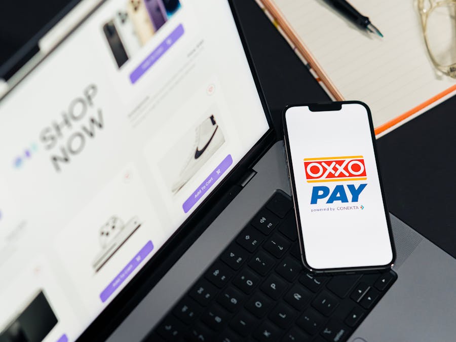 A mobile phone with OXXO Pay on a laptop used for online shopping.