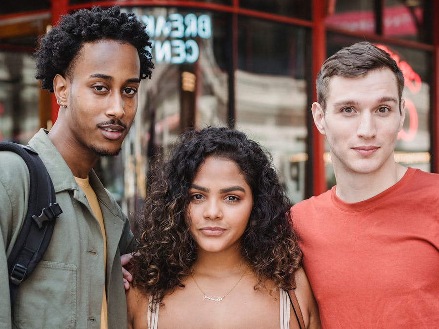 Content multiethnic group of friends looking at camera and hugging while standing on street near red modern house in city