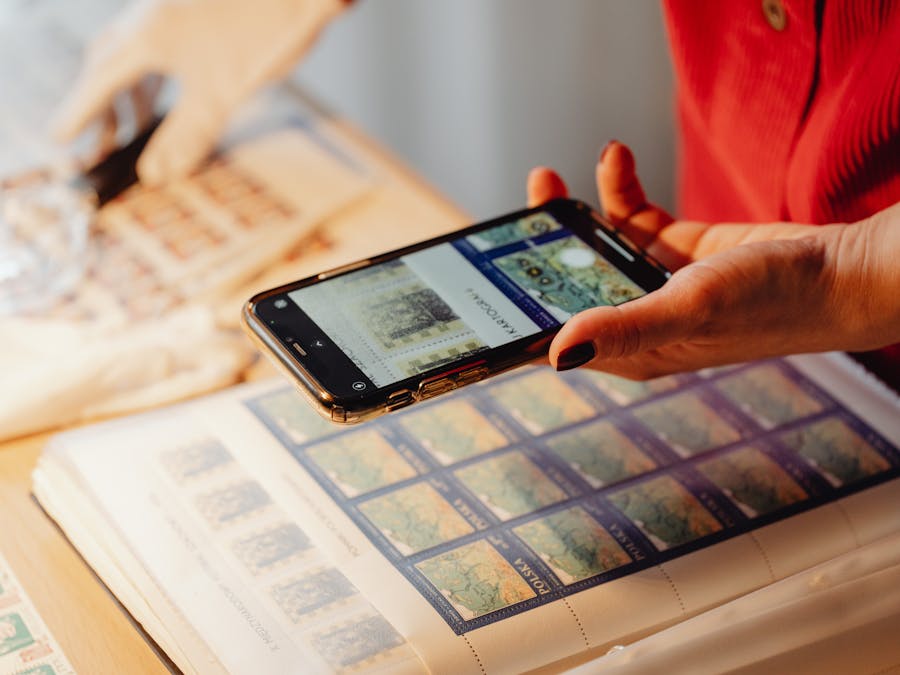 Individual photographing a stamp collection using a smartphone for cataloging.