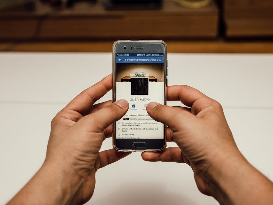 Close-up of hands using a smartphone with a social media page indoors.