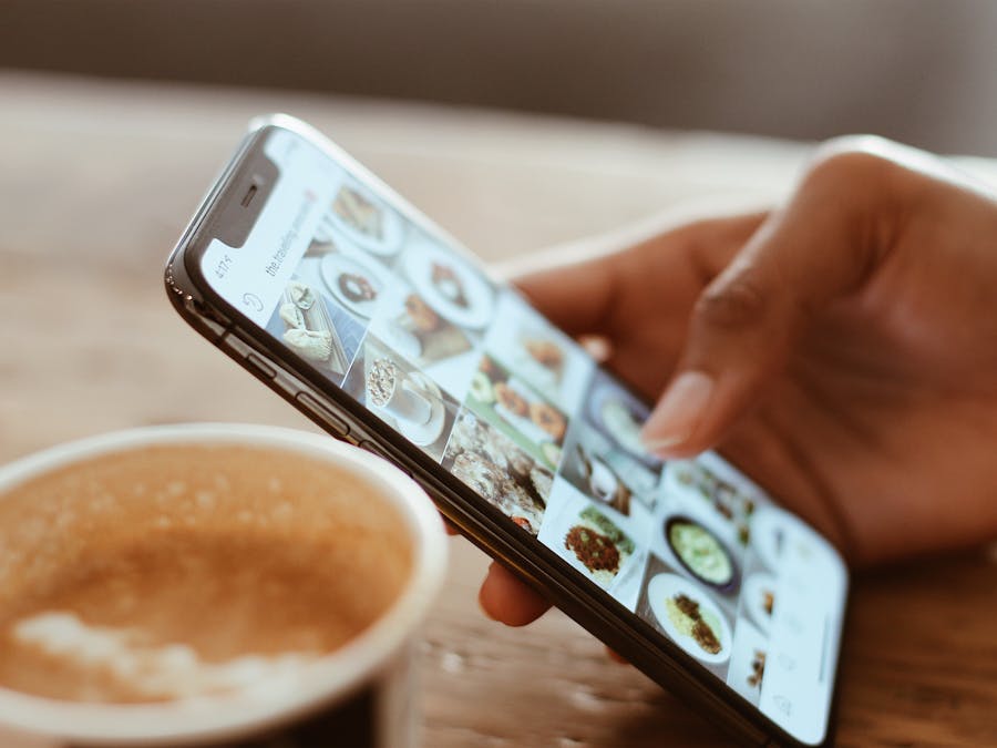 Hand browsing social media photos on a smartphone next to a cup of coffee indoors.
