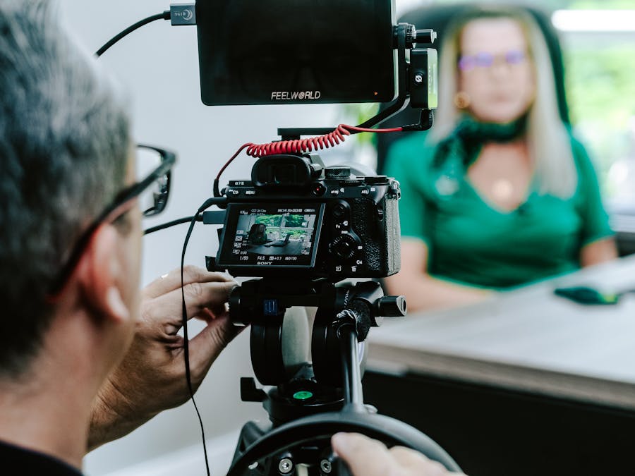 Close-up of a videographer filming a woman in an office setting, highlighting professional equipment.