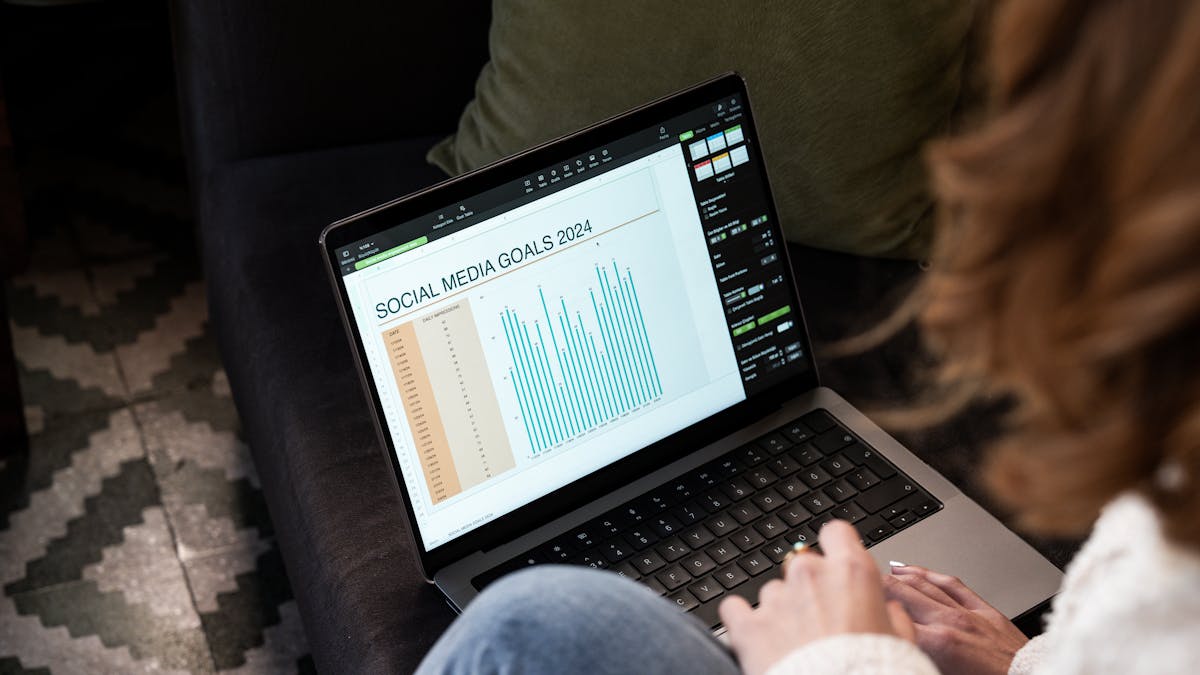 A woman reviewing 2024 social media goals on a laptop at home.